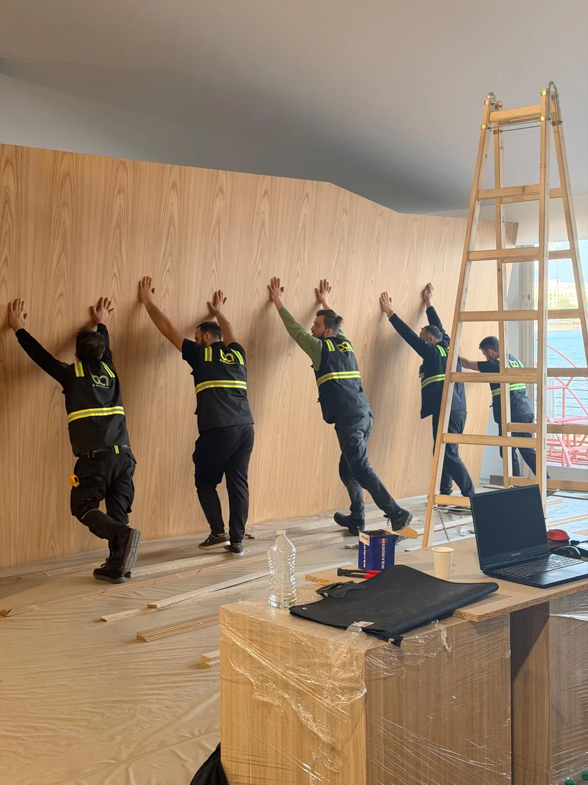 Ekip büyük bir ahşap duvar panelini birlikte hizalarken